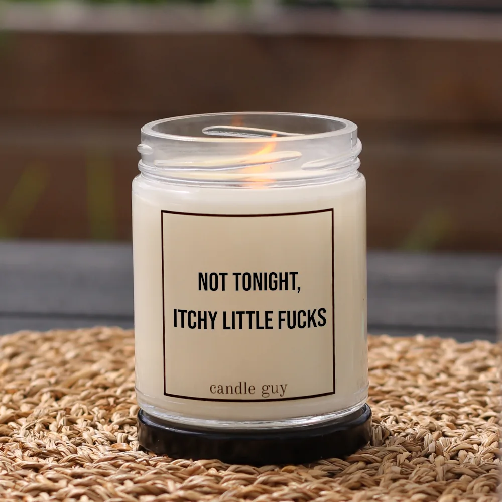 Brennende Anti-Mücken-Kerze mit dem Spruch „Not tonight, itchy little fucks“ im weißen Glas in gemütlicher Umgebung